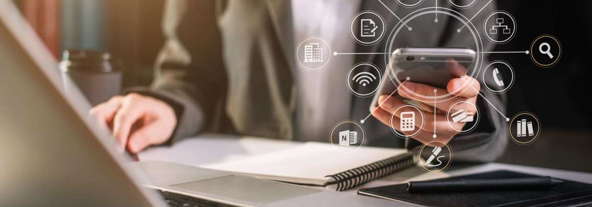 Mitarbeiter mit Handy vor dem Notebook mit symolischer Darstellung verschiedener Apps für den Arbeitsplatz
