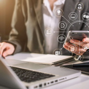 Mitarbeiter mit Handy vor dem Notebook mit symolischer Darstellung verschiedener Apps für den Arbeitsplatz