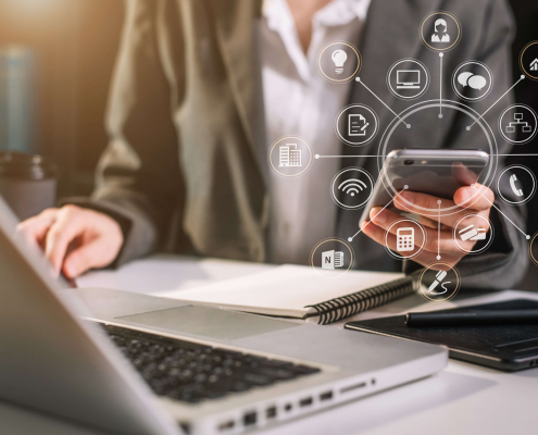 Mitarbeiter mit Handy vor dem Notebook mit symolischer Darstellung verschiedener Apps für den Arbeitsplatz