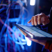 Ein IT-Mitarbeiter vor Kabelgewirr recherchiert die Begriffe "Hyperscaler vs. Cloud-Service-Provider" auf einem Tablet