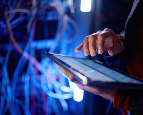 Ein IT-Mitarbeiter vor Kabelgewirr recherchiert die Begriffe "Hyperscaler vs. Cloud-Service-Provider" auf einem Tablet